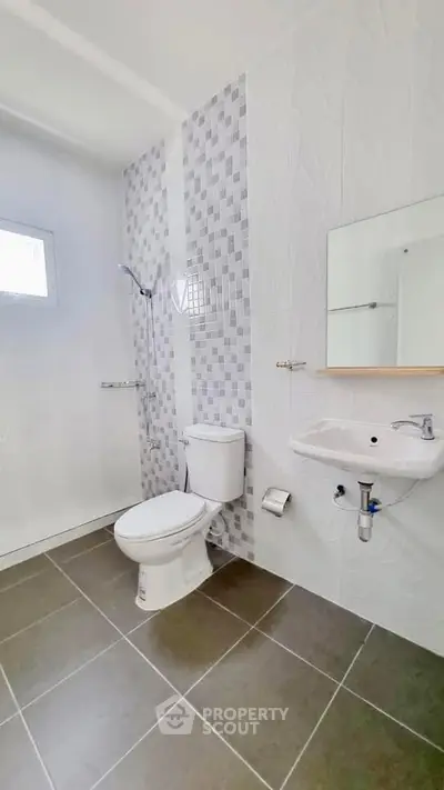 Modern bathroom with tiled walls and floor, featuring a toilet and sink.