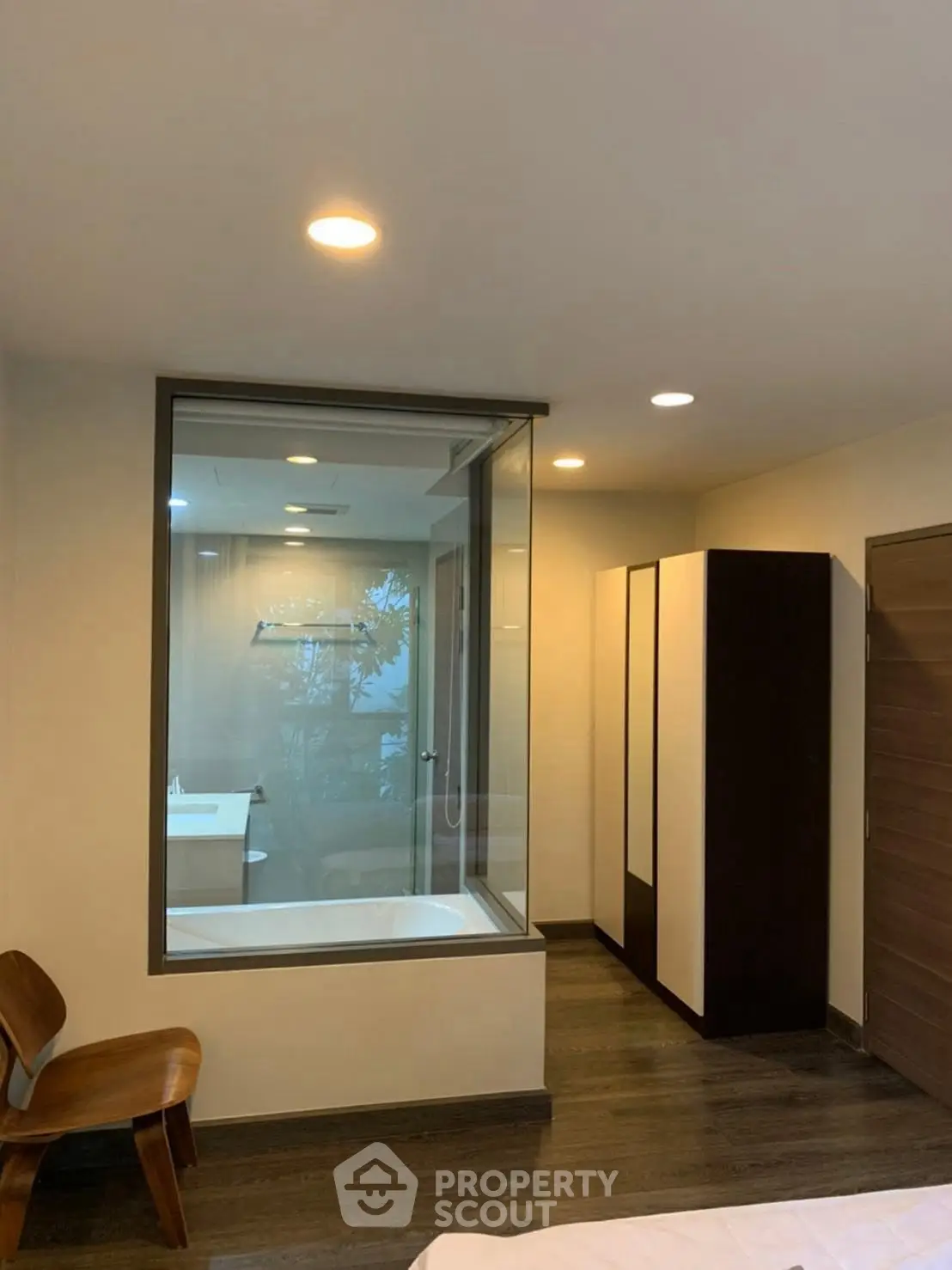 Modern bedroom with glass wall view into luxurious bathroom featuring a sleek bathtub.