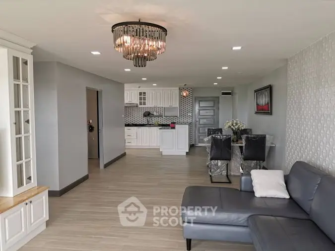 Elegant open-concept living space with modern kitchen, chic chandelier, and stylish furnishings, perfect for entertaining and comfortable living.