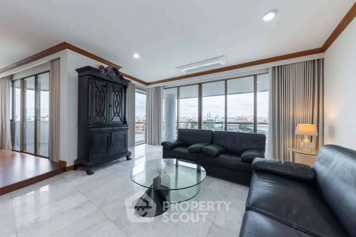 Spacious living room with city view, elegant black leather sofas, and floor-to-ceiling windows.
