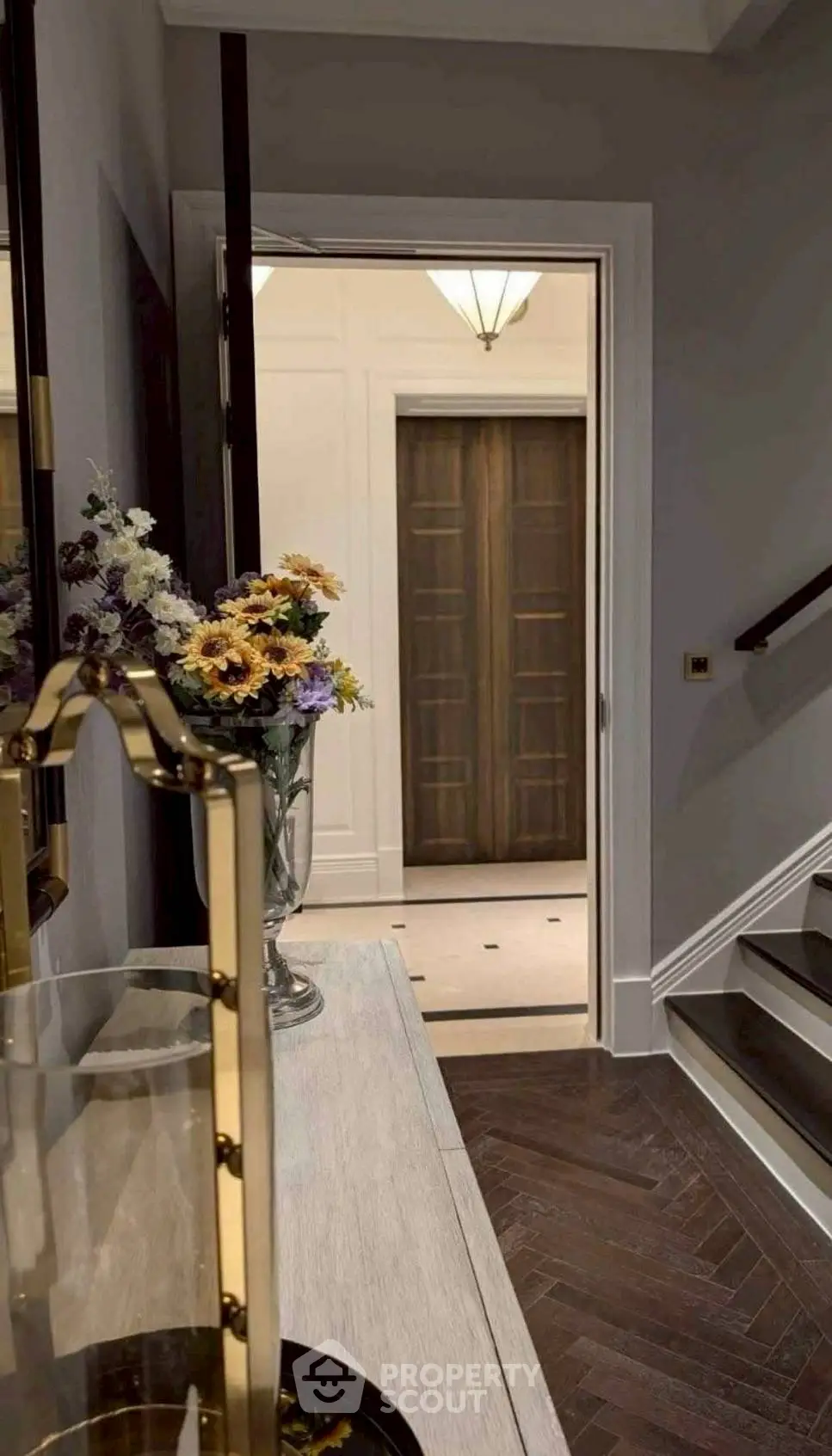 Elegant hallway with stylish decor leading to a modern elevator, featuring a vase of flowers and chic lighting.
