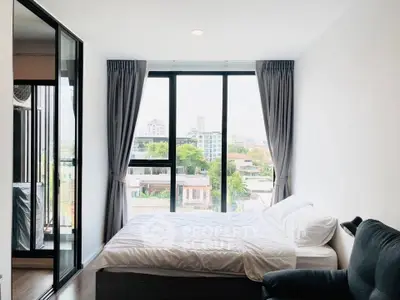 Bright bedroom with large window offering city view, modern furnishings, and cozy ambiance.