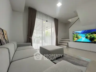Modern living room with sleek gray sofa, large TV, and floor-to-ceiling windows opening to a patio.