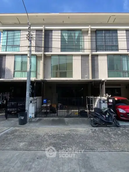 Modern three-story townhouse with large windows and parking space in urban setting.