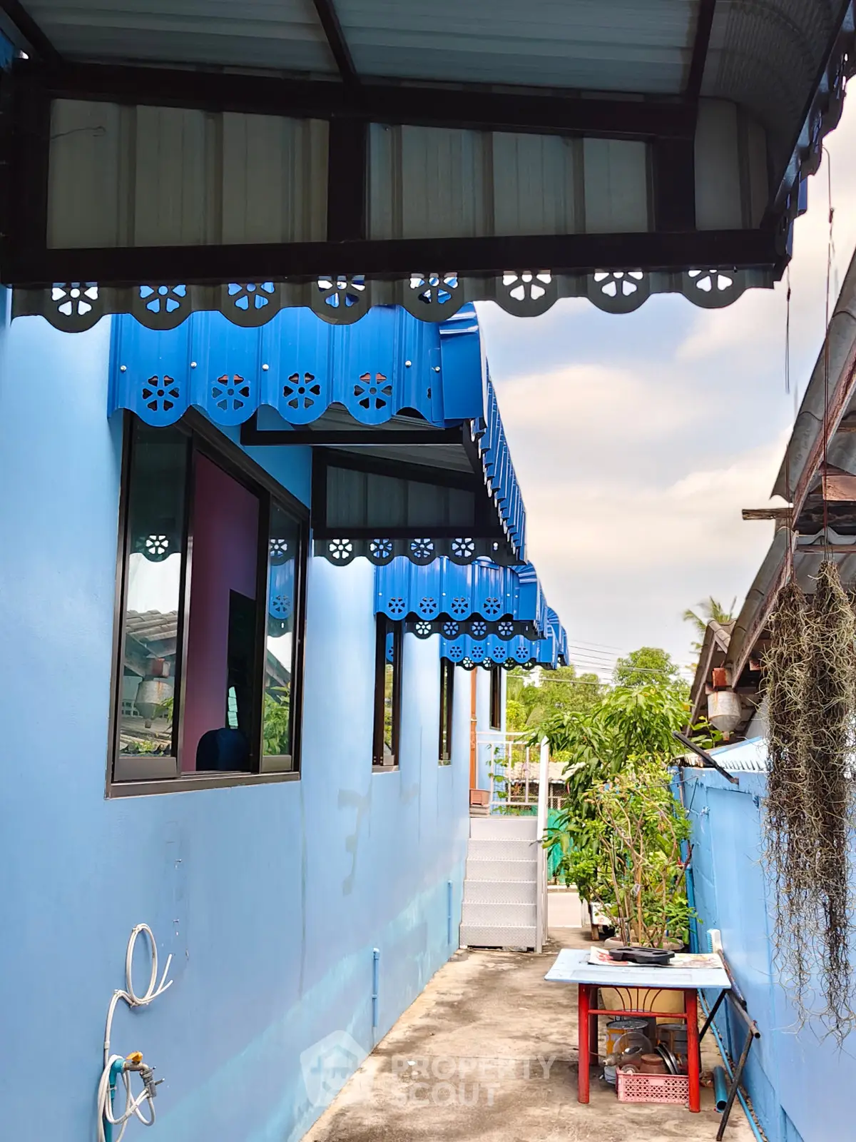 Charming blue exterior with decorative awnings and lush greenery in a cozy residential setting.
