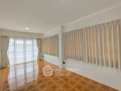 Spacious empty room with tiled floor and large windows with curtains, perfect for customization.