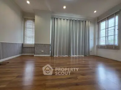 Spacious empty room with wooden flooring and large windows, perfect for customization.