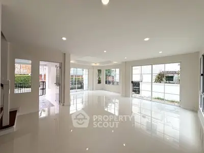 Spacious modern living room with large windows and glossy floors, offering abundant natural light and garden views.