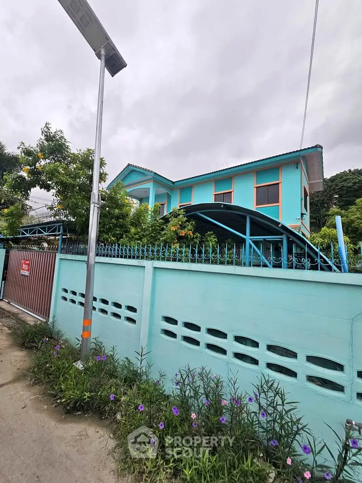 Charming turquoise house with lush garden and secure gated entrance, perfect for serene living.