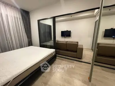 Modern bedroom with glass partition and cozy living area, featuring sleek design and neutral tones.