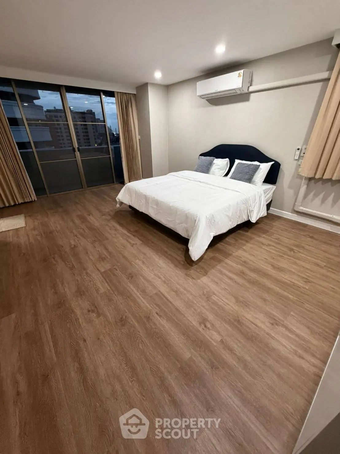 Spacious bedroom with wooden flooring and large windows offering city views.