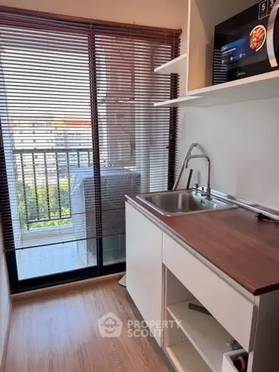 Compact kitchen with balcony view and modern appliances in urban apartment.