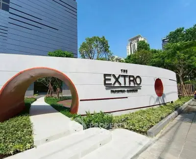 Modern building entrance with stylish signage and lush landscaping in urban setting.