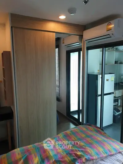 Modern bedroom with sliding door closet and air conditioning, adjacent to a compact kitchen.
