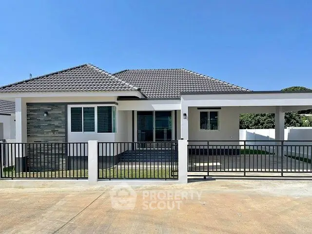 Modern single-story house with tiled roof and fenced yard under clear blue sky.
