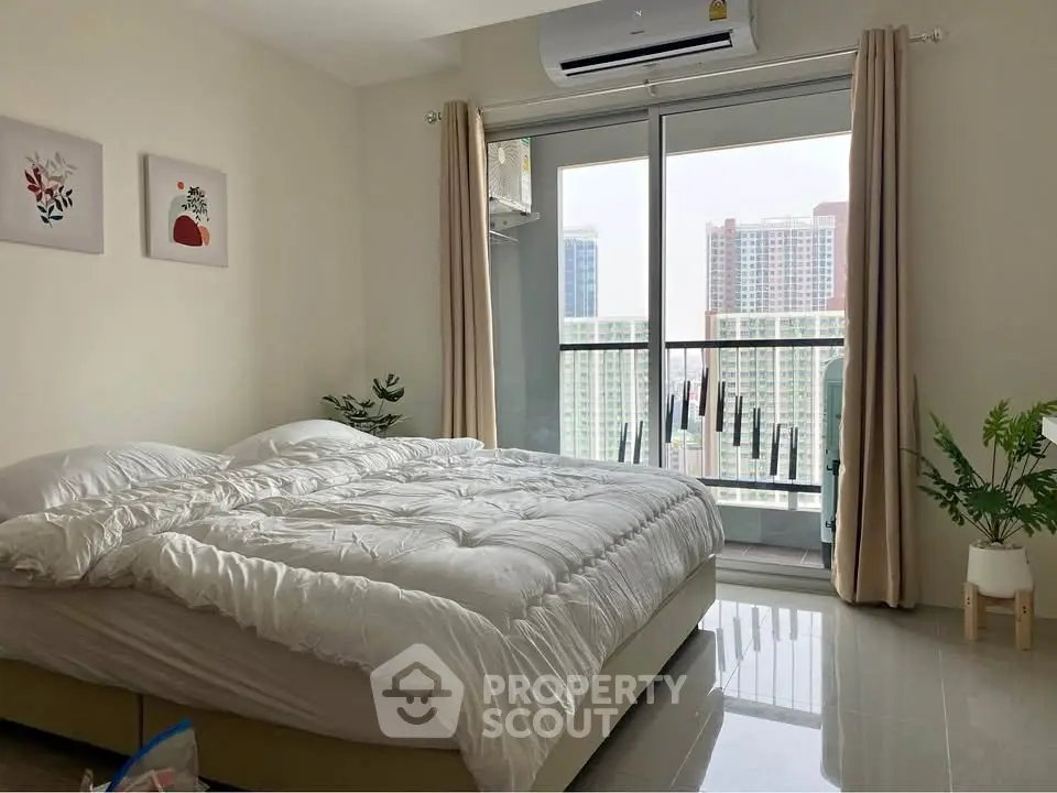 Spacious bedroom with modern decor and city view balcony in high-rise apartment.