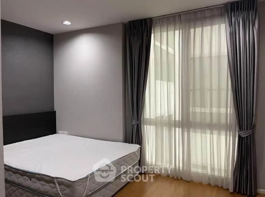 Spacious bedroom with large window and elegant curtains in modern apartment.