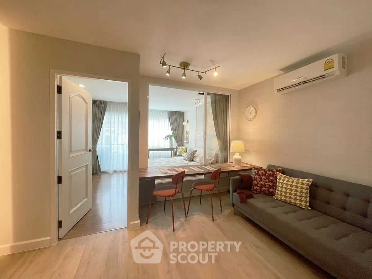Modern living room with stylish decor and cozy seating area, featuring a view into a bright bedroom.