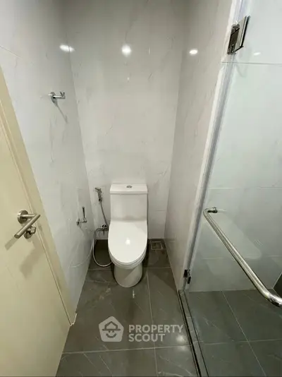 Modern bathroom with sleek design and glass shower door, featuring a contemporary toilet and marble tiles.