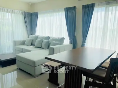 Spacious living room with elegant sofa and dining area, featuring large windows and natural light.