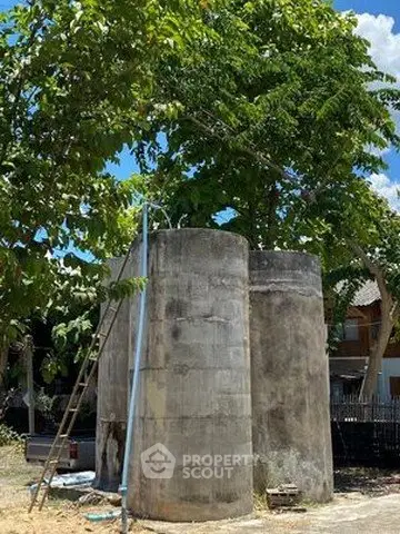 Concrete water tanks in a residential backyard with lush greenery and clear blue sky.