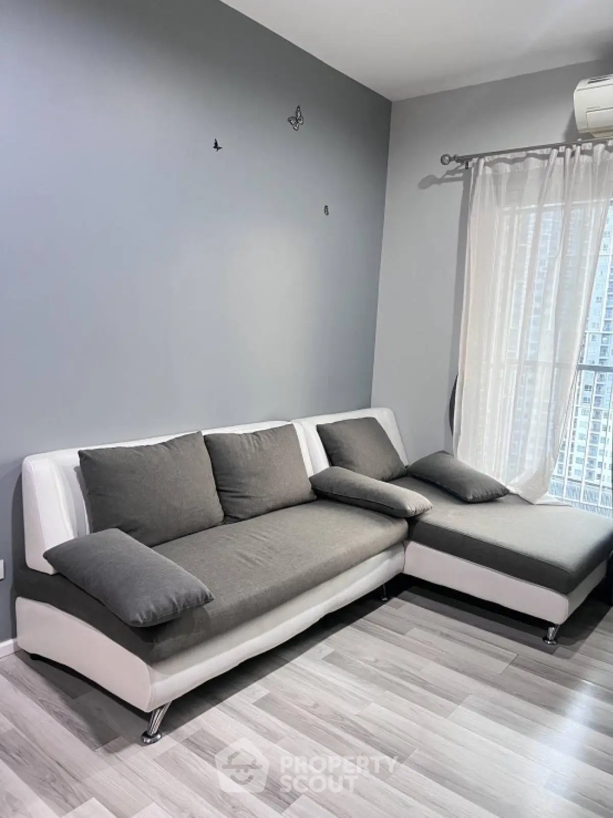 Modern living room with stylish gray sectional sofa and large window with city view.