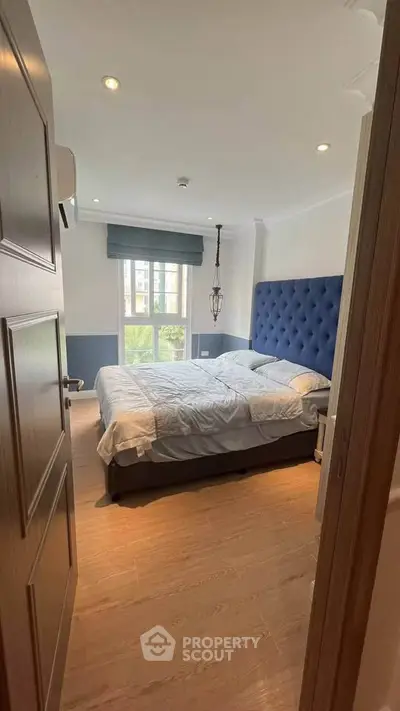 Cozy bedroom with elegant blue headboard and natural light from large window.