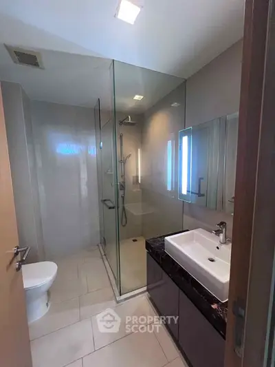 Modern bathroom with glass shower and sleek vanity in contemporary apartment.