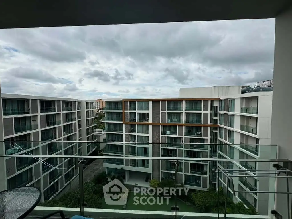 Modern apartment complex with glass balconies and lush courtyard view.
