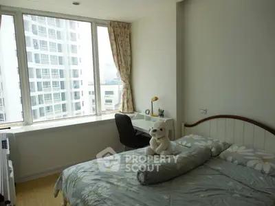 Cozy bedroom with large window and city view, featuring a study desk and plush decor.