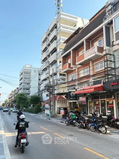 Street view of urban residential buildings with balconies and parked motorcycles.