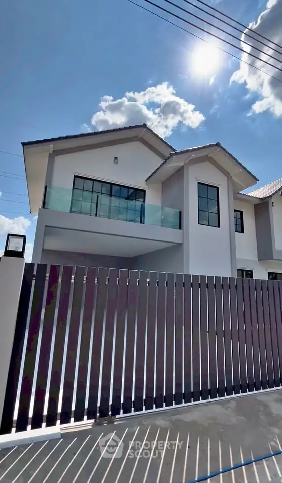 Modern two-story house with sleek balcony and gated entrance under a bright blue sky.