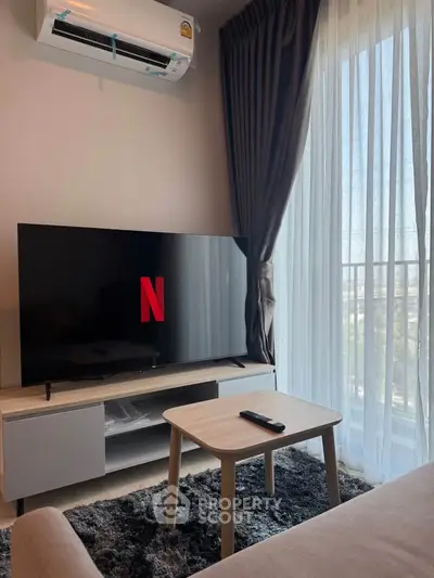 Modern living room with TV, air conditioning, and natural light from large window.