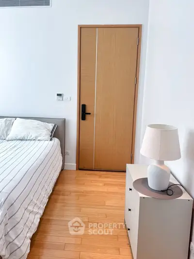 Modern bedroom with wooden flooring, stylish bed, and elegant lamp on a nightstand.