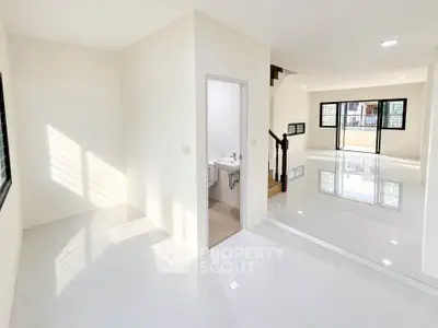 Spacious modern living room with glossy white tiles and natural light, featuring a small bathroom.