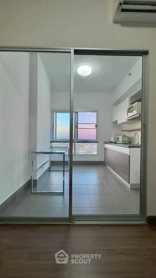 Modern kitchen with glass sliding doors and city view, featuring sleek cabinetry and tiled flooring.