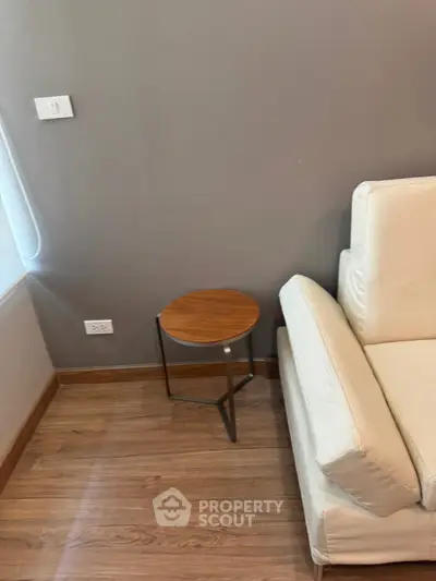 Modern living room corner with beige sofa and wooden side table on hardwood floor.