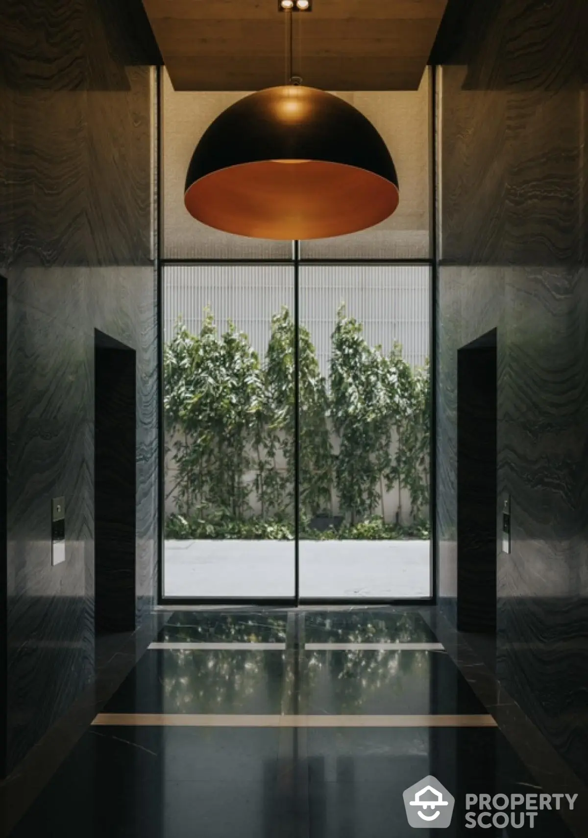 Elegant modern building entrance with stylish lighting and lush greenery view.