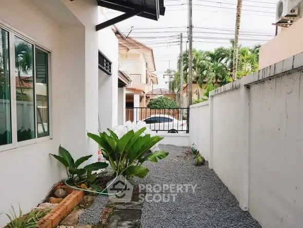 Charming side garden with lush greenery and gravel path leading to a gated entrance.