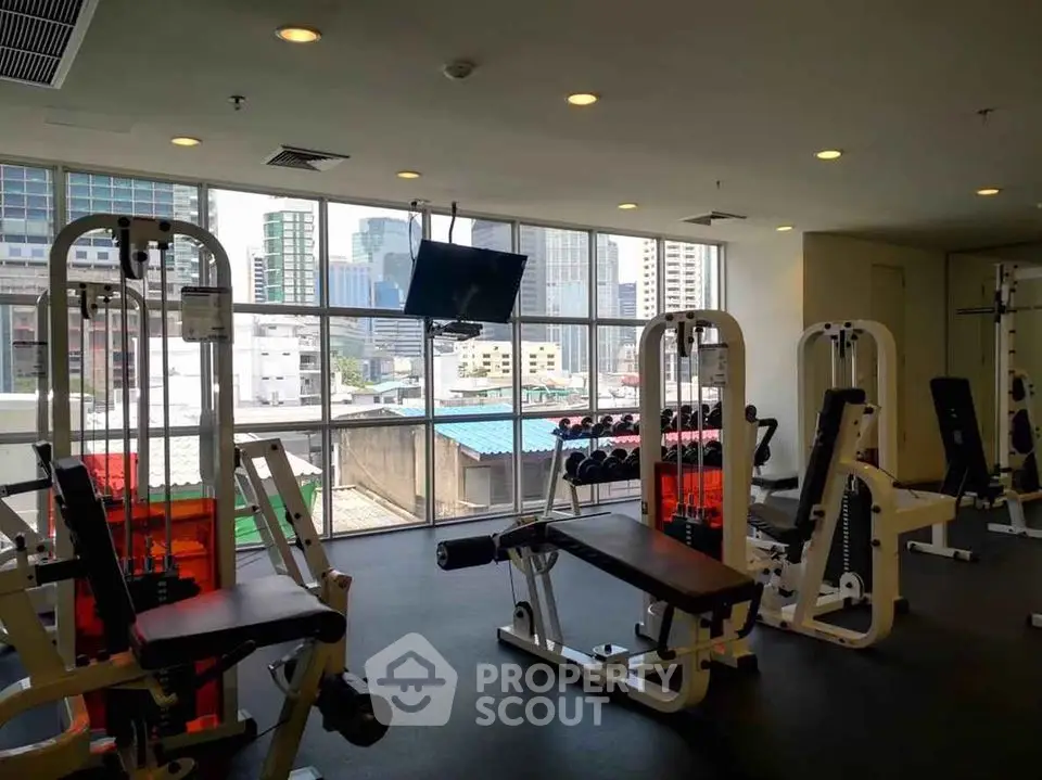 Spacious gym with modern equipment and city view in luxury apartment building.
