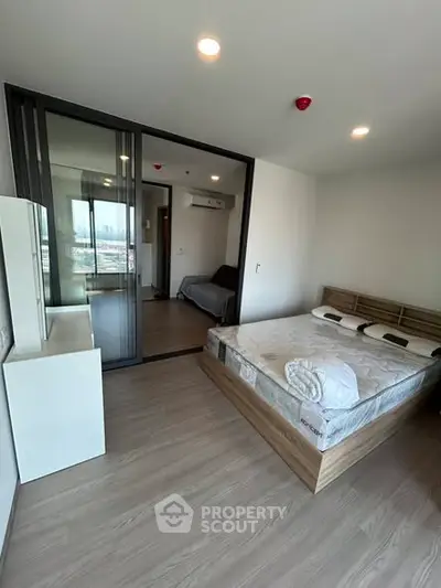 Modern bedroom with wooden flooring and large window, featuring a comfortable bed and sleek furniture.