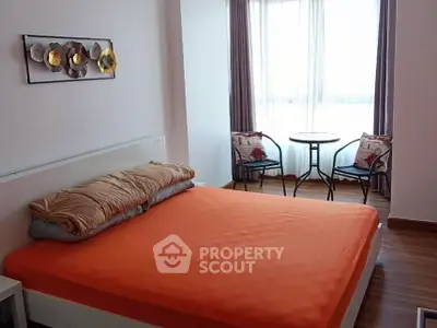 Cozy bedroom with bright orange bedding and charming seating area by the window.