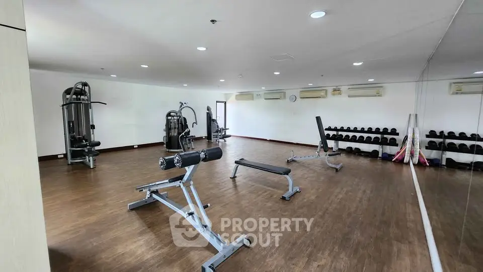 Spacious gym with modern fitness equipment and mirrored wall in a residential building.
