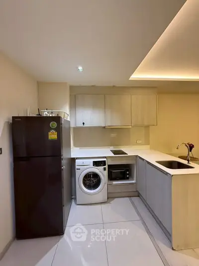 Modern kitchen with sleek appliances and open layout, featuring a washing machine and microwave.