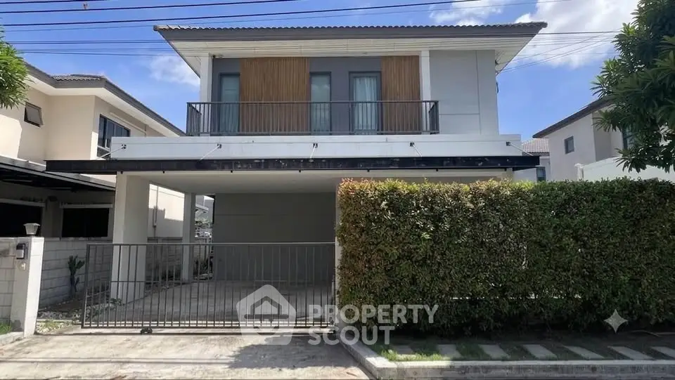 Modern two-story house with balcony and gated driveway in suburban neighborhood.