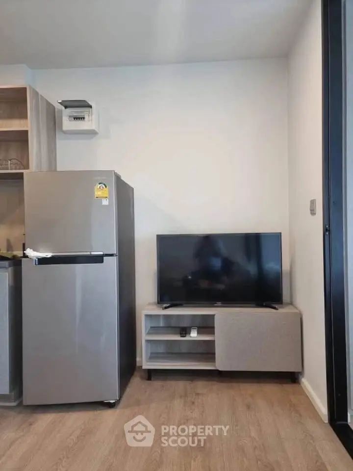 Modern apartment interior with sleek fridge and flat-screen TV on wooden flooring.