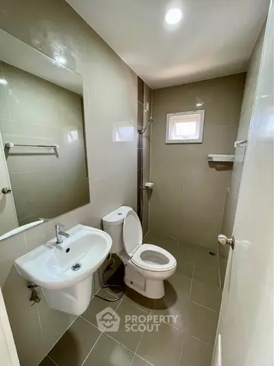 Modern bathroom with sleek fixtures and neutral tiles, featuring a compact design and efficient layout.