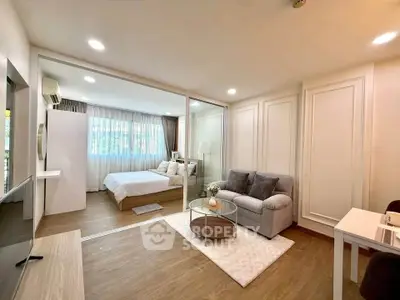 Modern studio apartment with open layout, featuring cozy living area and elegant bedroom separated by glass partition.
