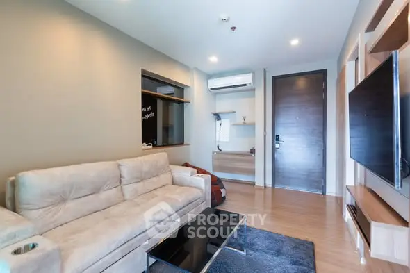 Modern living room with beige sofa, wall-mounted TV, and sleek wooden flooring.