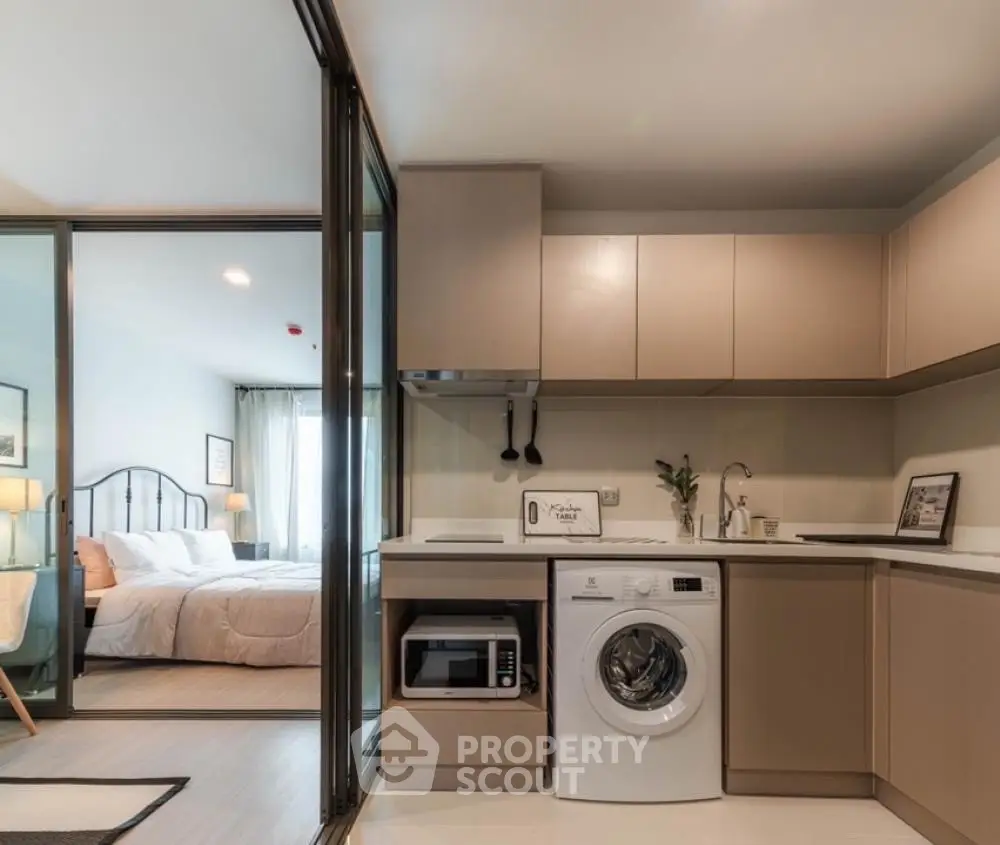 Modern apartment with sleek kitchen and cozy bedroom, featuring washing machine and microwave.